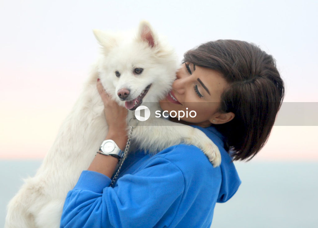 Woman in blue long sleeve shirt hugging white dog