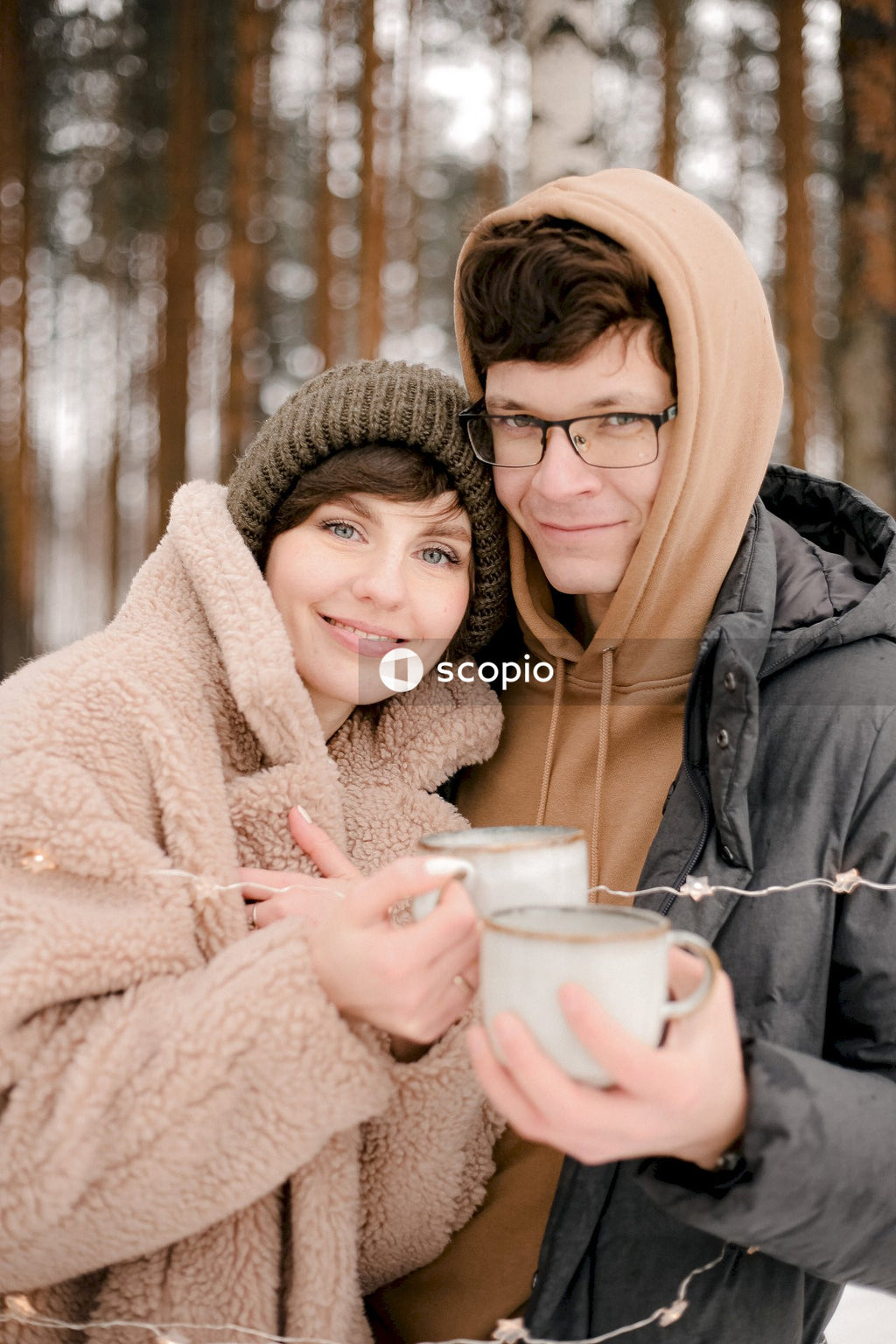Man and woman holding hot drinks standing in snow covered woods