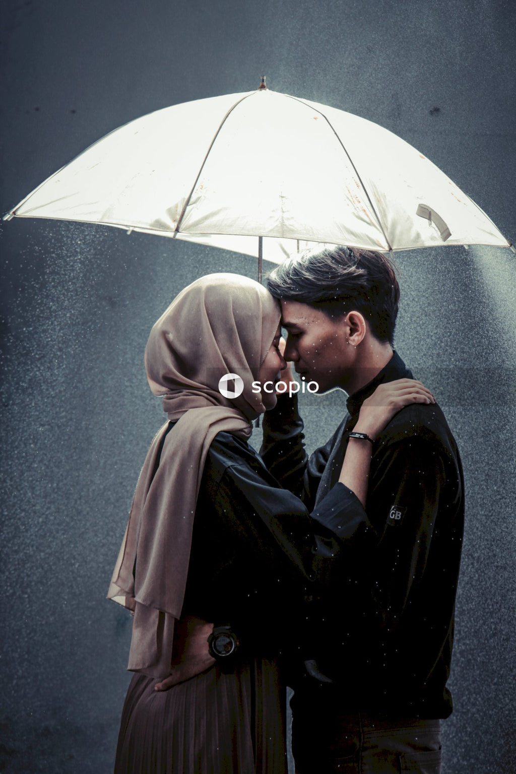 Woman in brown hijab and man hugging under umbrella