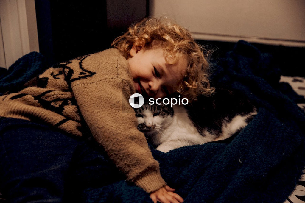 Woman in brown sweater hugging white and black cat