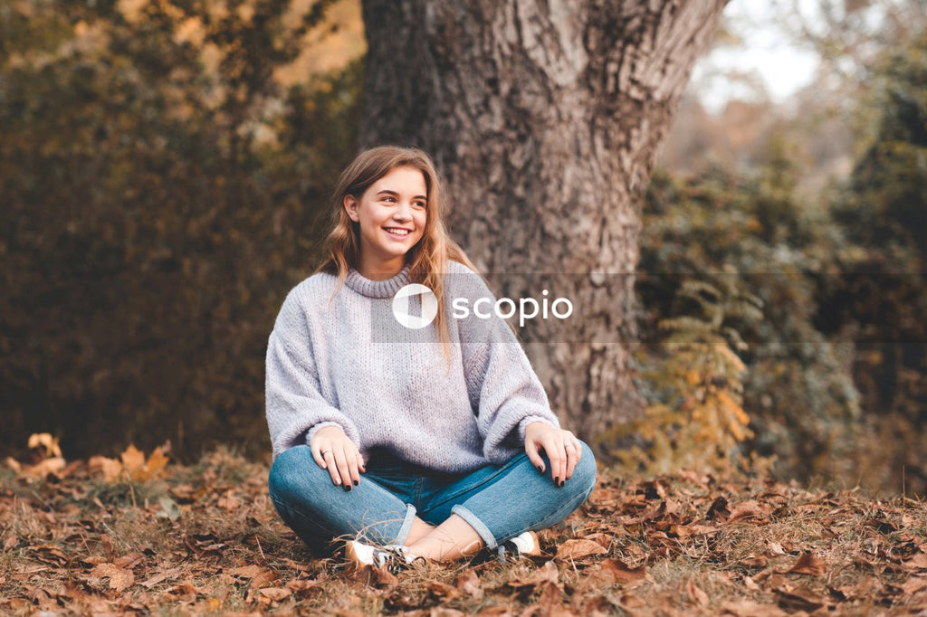 Woman in gray sweater and blue denim jeans sitting on brown tree trunk