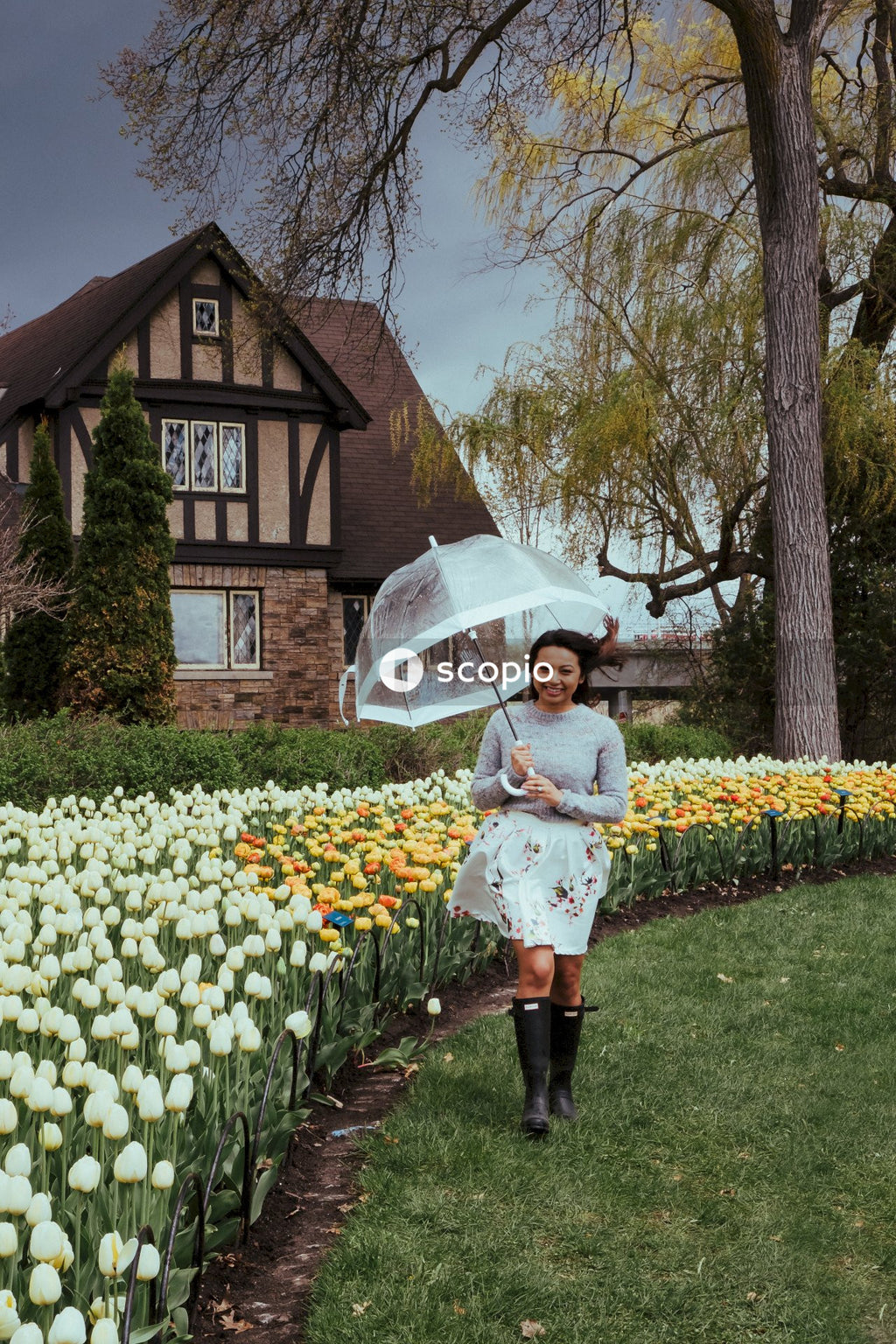 Woman in light dress holding umbrella walking in garden a beside house