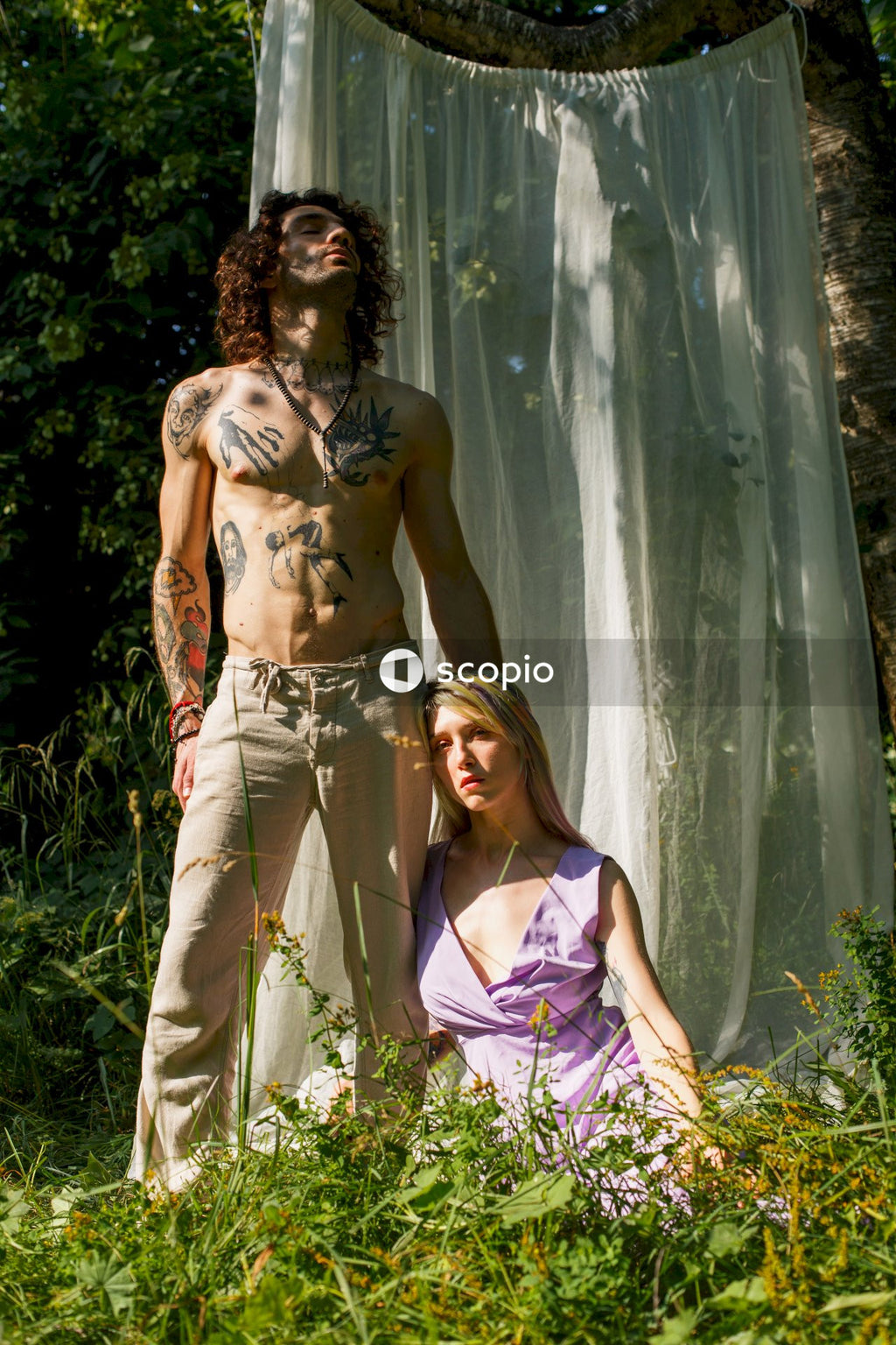 Woman in purple and white floral halter top and brown pants standing near green plants