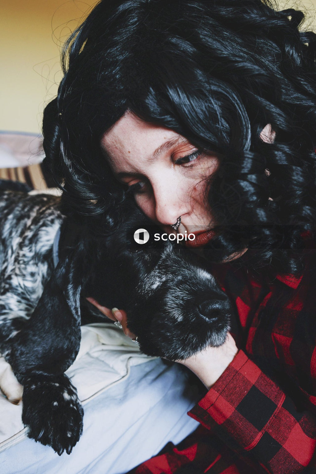 Woman in red and black plaid shirt hugging black and white short coated dog