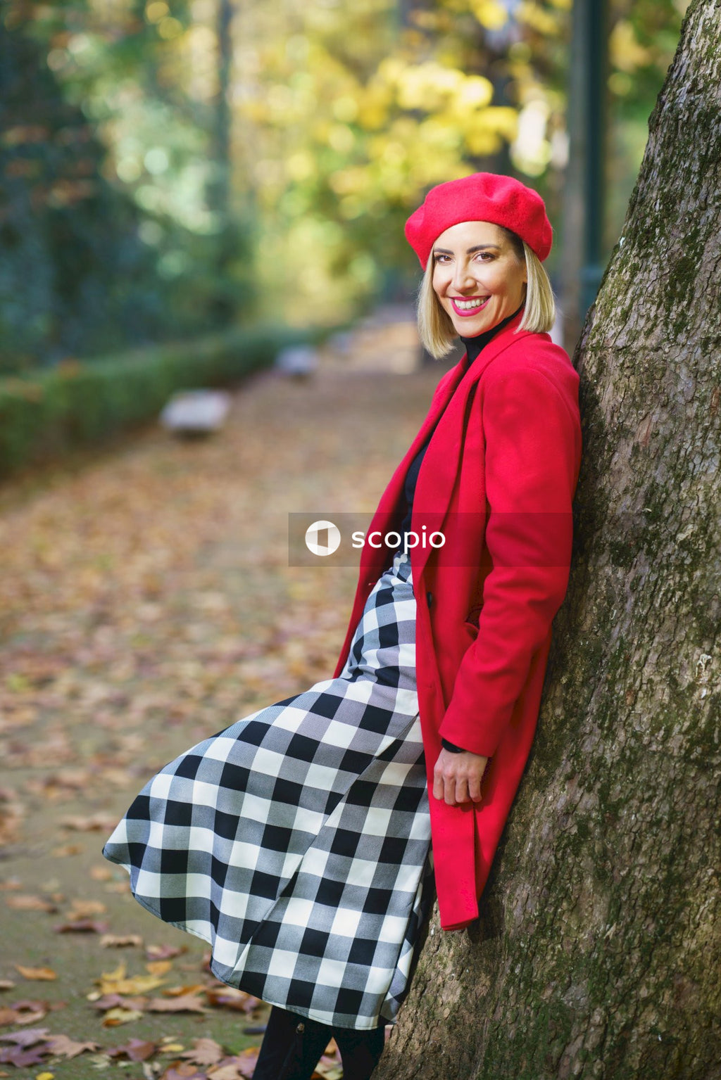 Woman in red coat leaning on tree