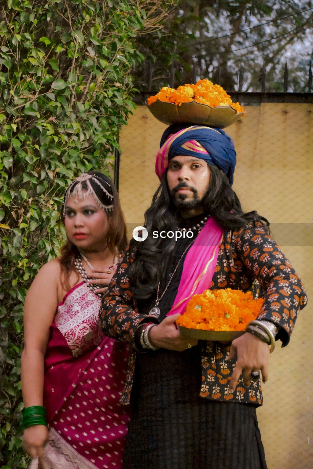 Indian couple holding baskets of marigold flowers standing outdoor