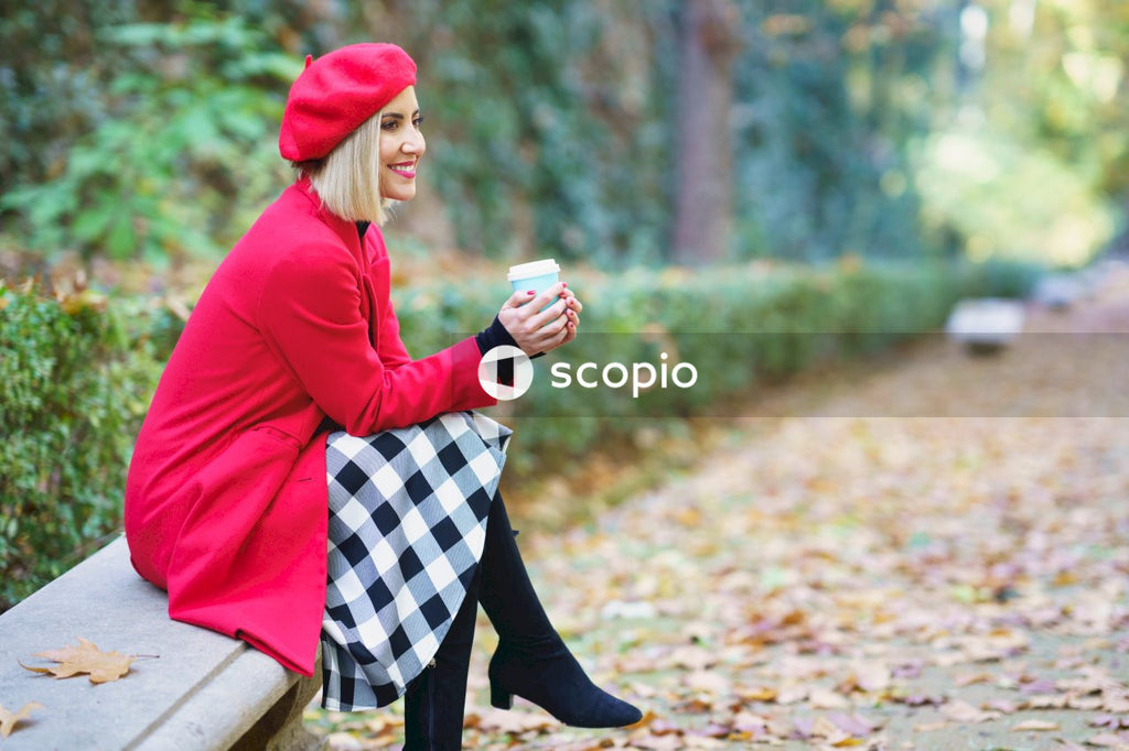 Woman in red hoodie and black and white striped skirt sitting on brown dried leaves