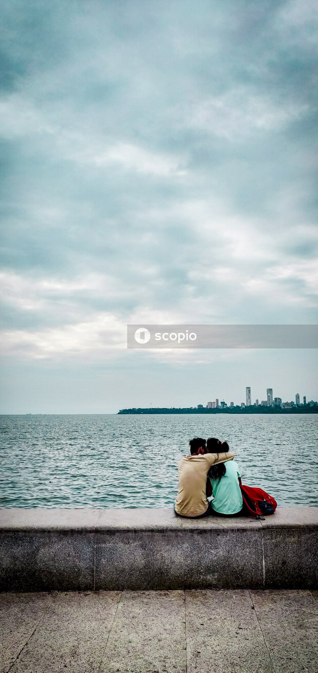 Man and woman hugging and sitting on concrete bench on seashore