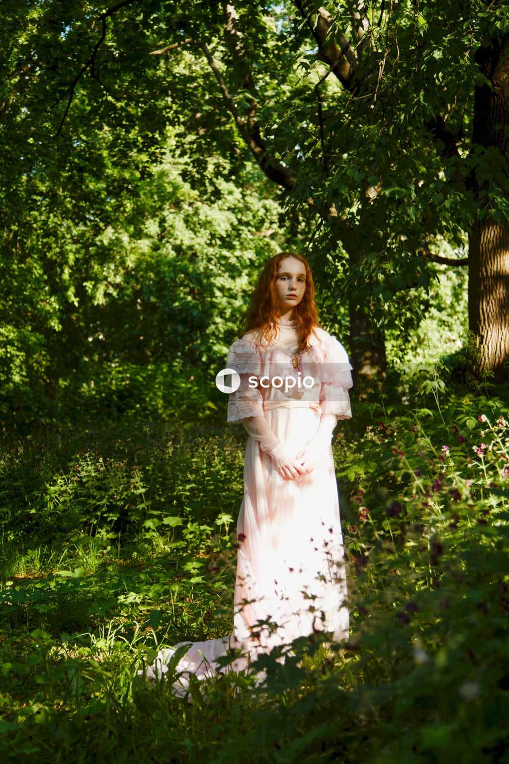 Woman in white and black floral dress standing near green trees