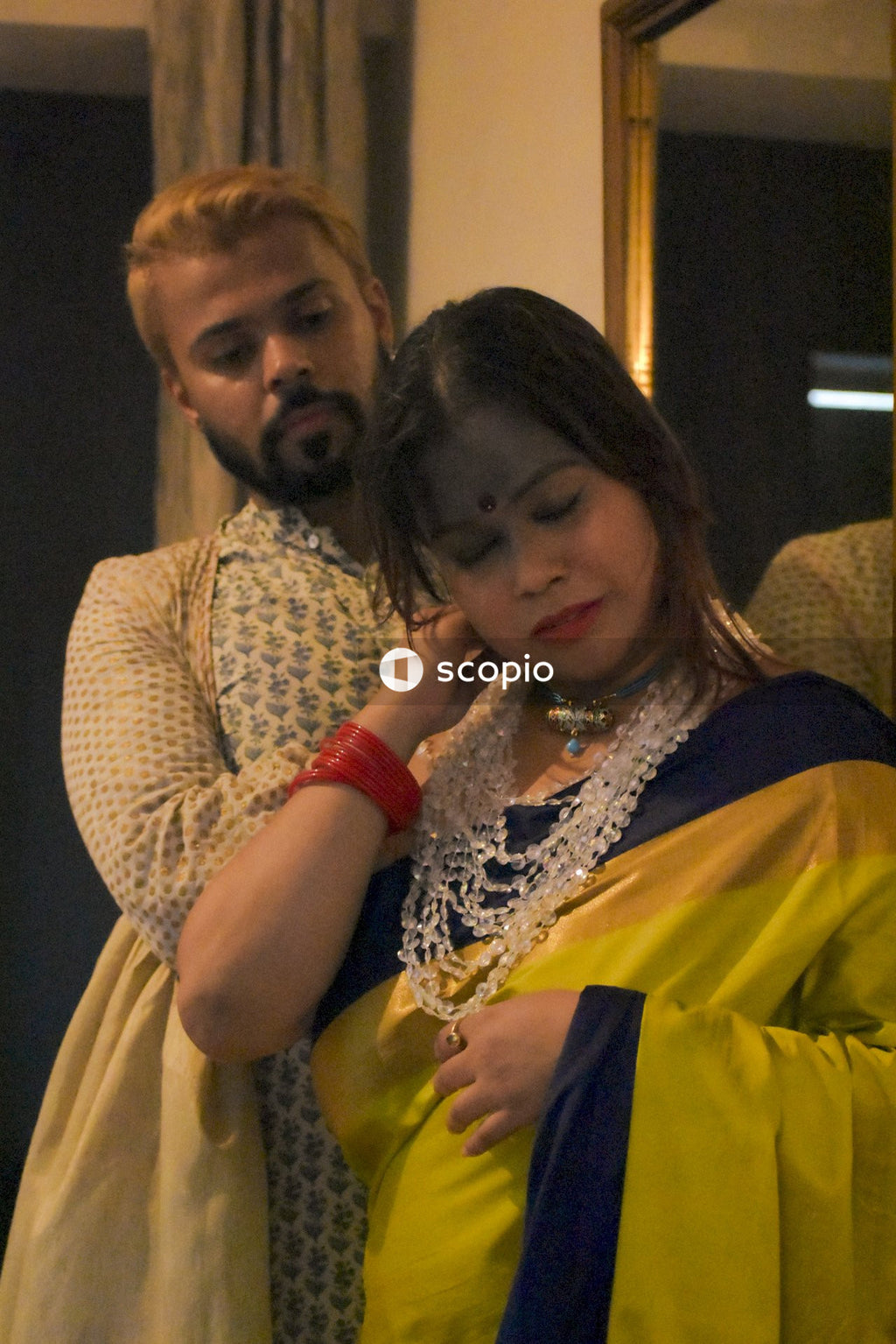Woman in yellow sari standing beside a man indoor