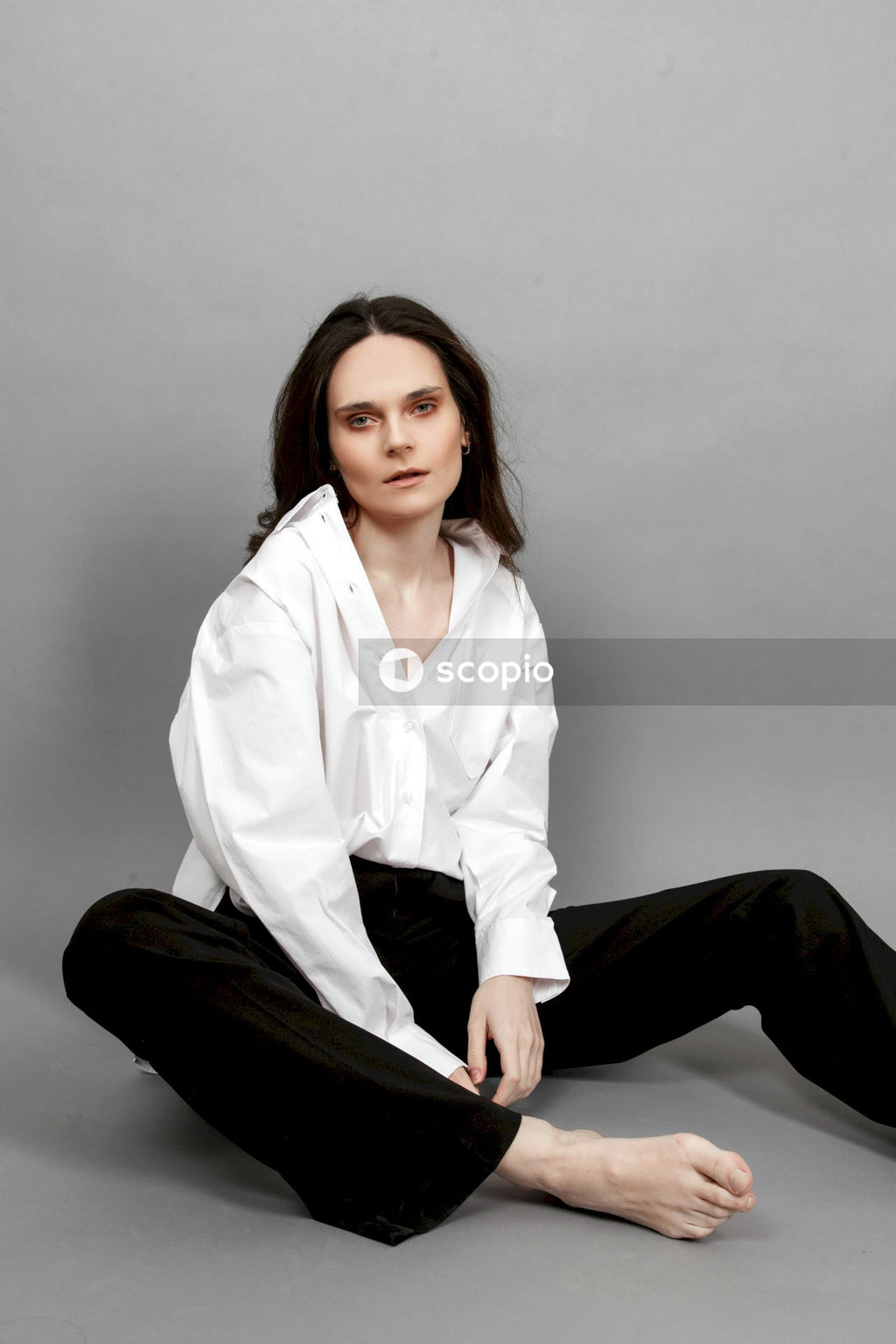 Woman in white button up long sleeve shirt and black pants sitting on floor