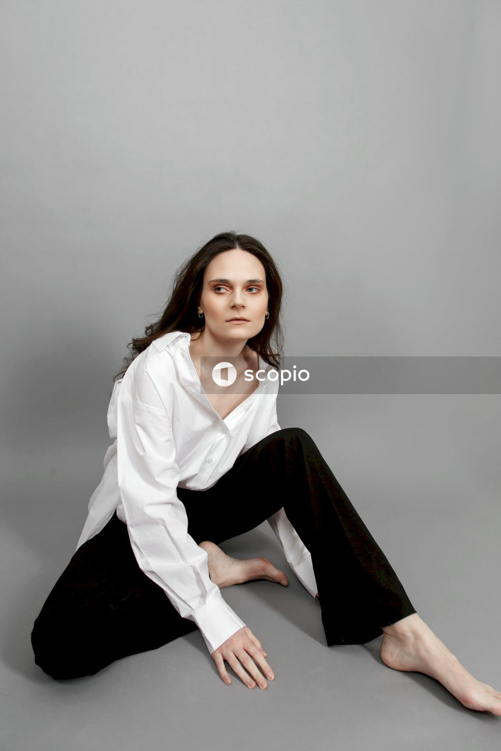 Woman in white dress shirt and black pants sitting on gray floor