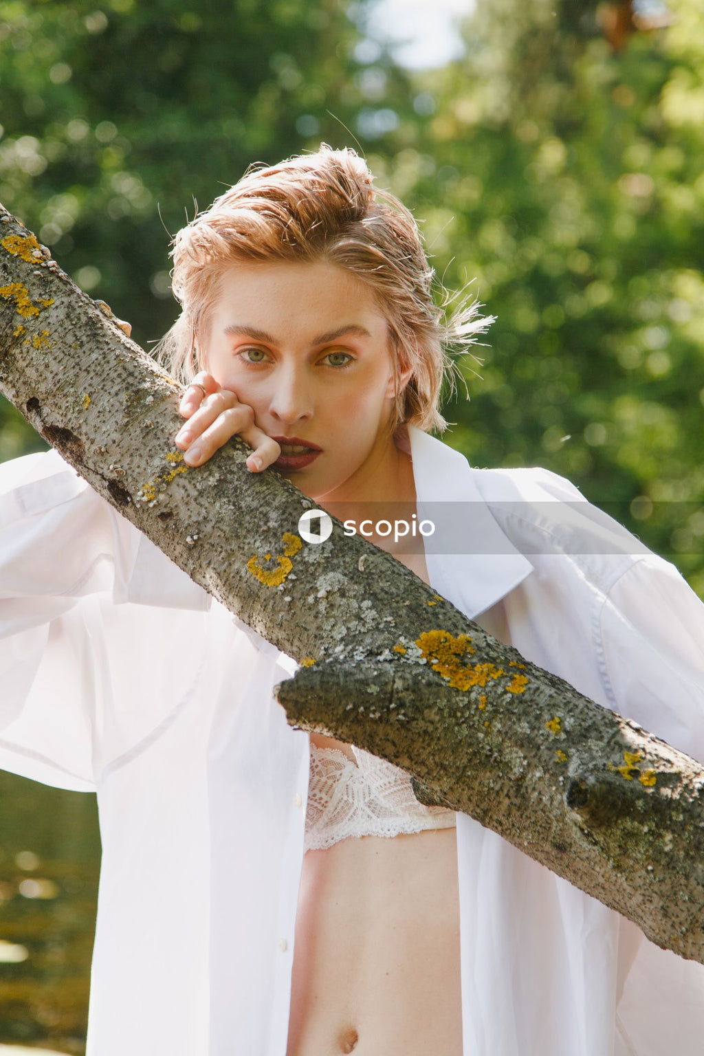 Woman in white dress shirt leaning on brown tree