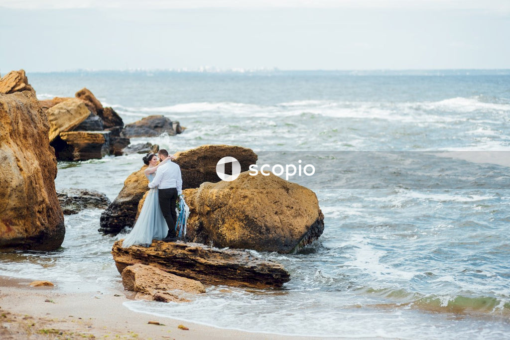 Man and woman hugging and standing on rock at the beach