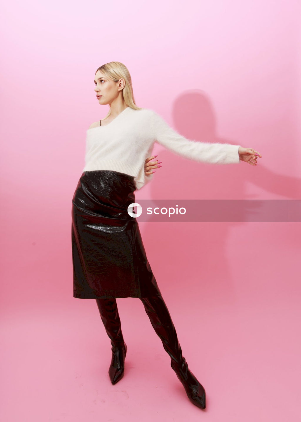 Woman in white long sleeve shirt and black skirt standing on pink background