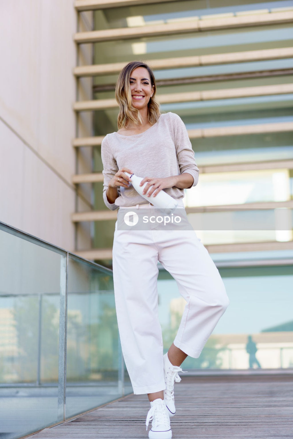 Woman in white long sleeve shirt and white pants standing on gray concrete stairs