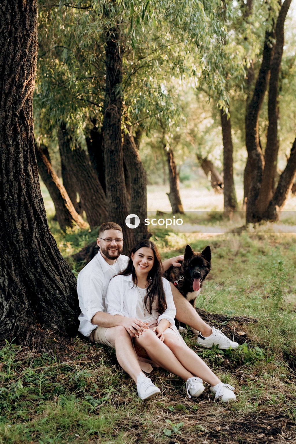 Man and woman and a dog sitting beside tree