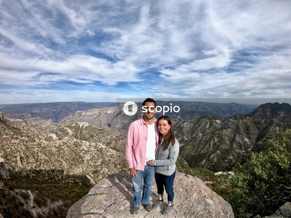 Man and woman standing side by side on rock near mountainous landform