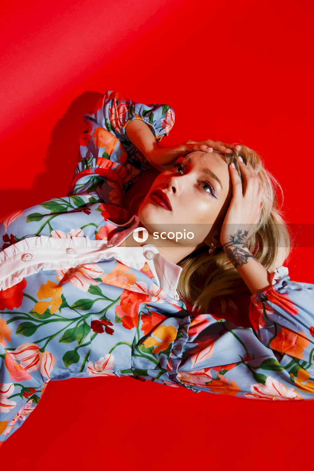 Woman in white red and green floral dress lying on red textile