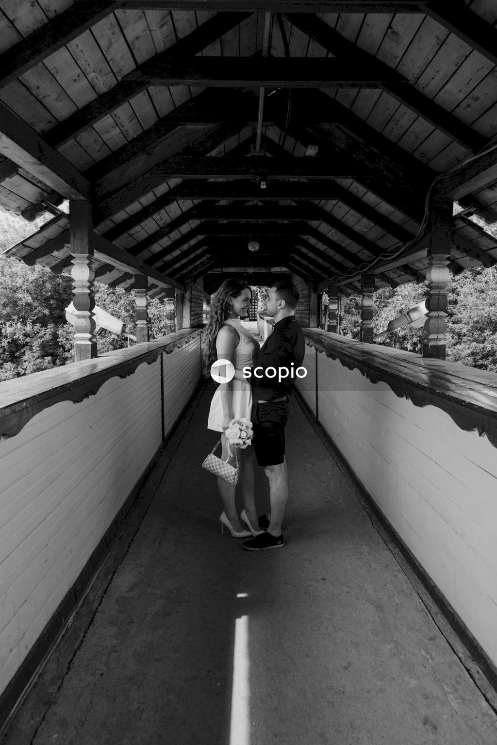 Grayscale photo of man and woman hugging each other on bridge