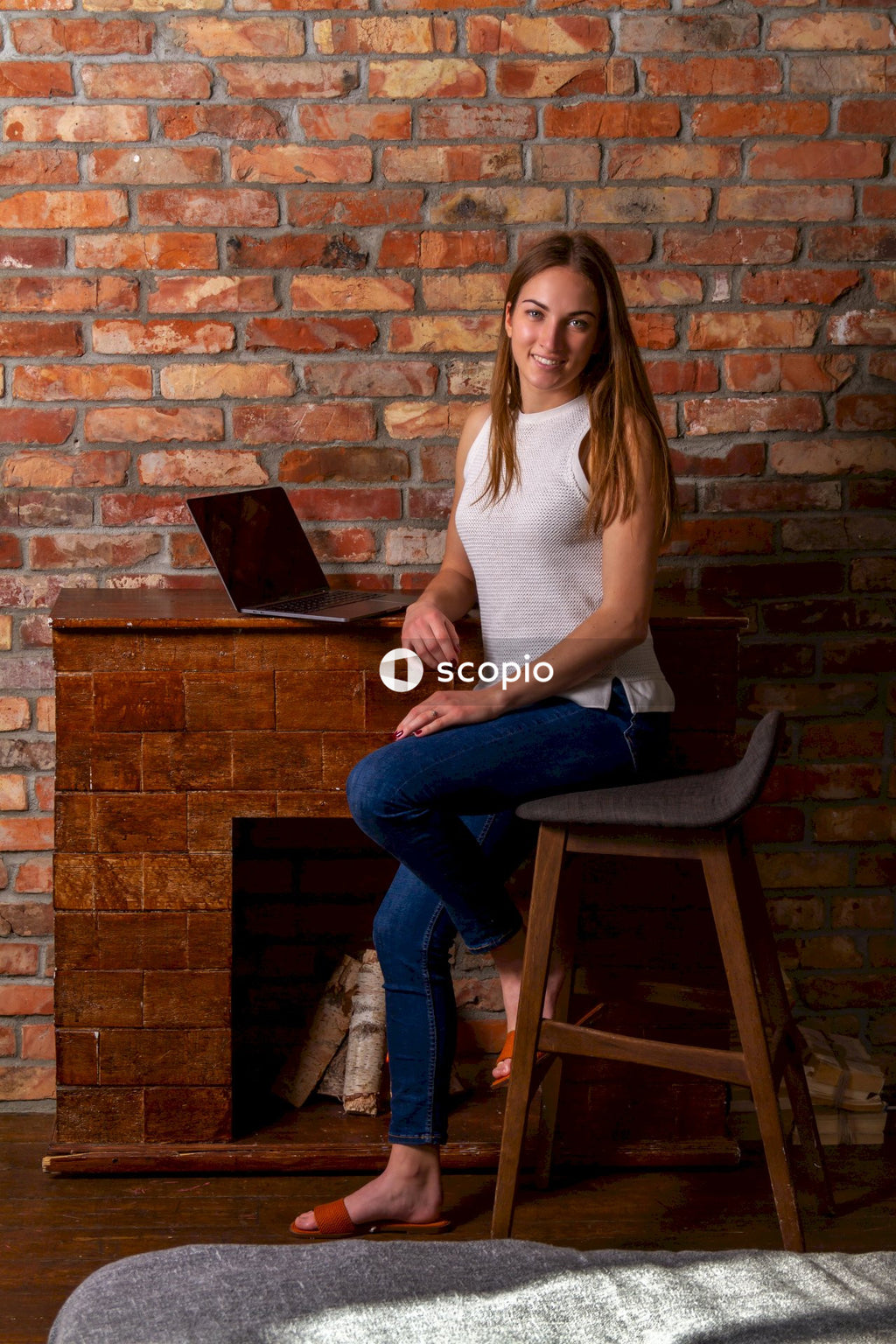 Woman in white tank top and blue denim jeans sitting on brown wooden chair