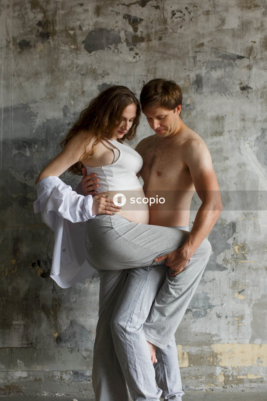 Woman in white tank top hugging man in gray pants