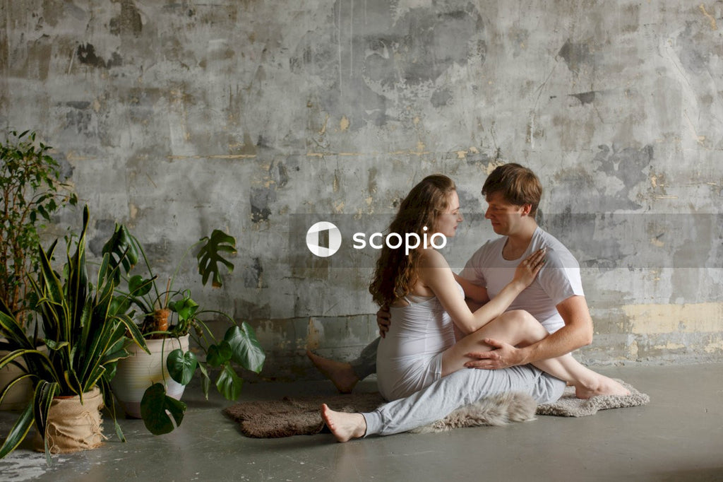 Woman in white tank top sitting on brown wooden floor with a man