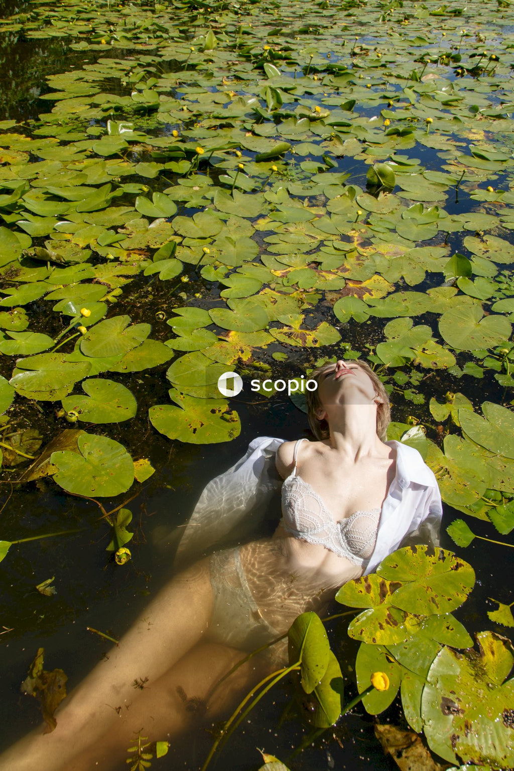 Woman in white tank top sitting on water with green leaves