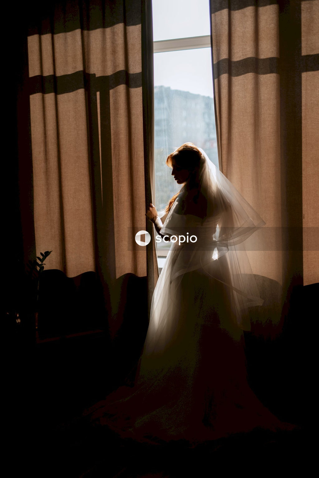 Woman in white wedding dress standing near window