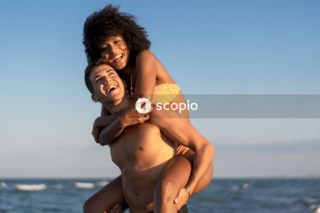 Woman in yellow bikini top hugging man in blue denim jeans near sea