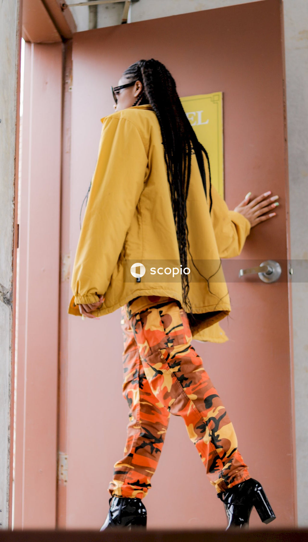 Woman in yellow jacket and orange pants standing beside door