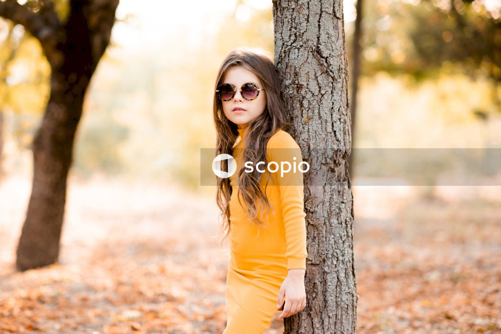 Woman in yellow long sleeve shirt wearing black sunglasses standing beside brown tree