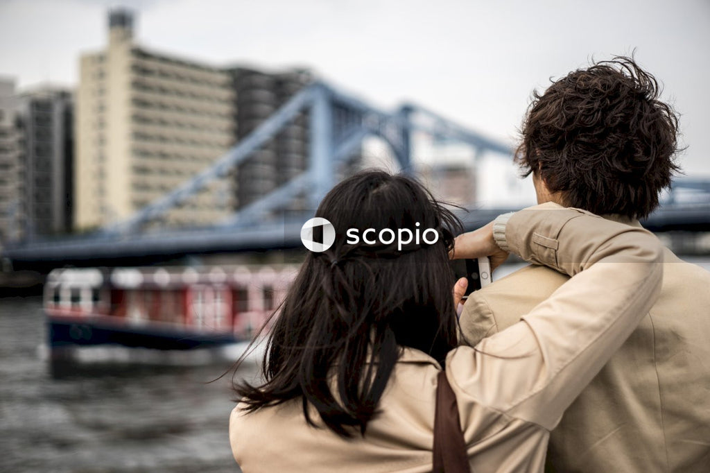 Woman leaning on a man and holding a smartphone looking at bridge in city