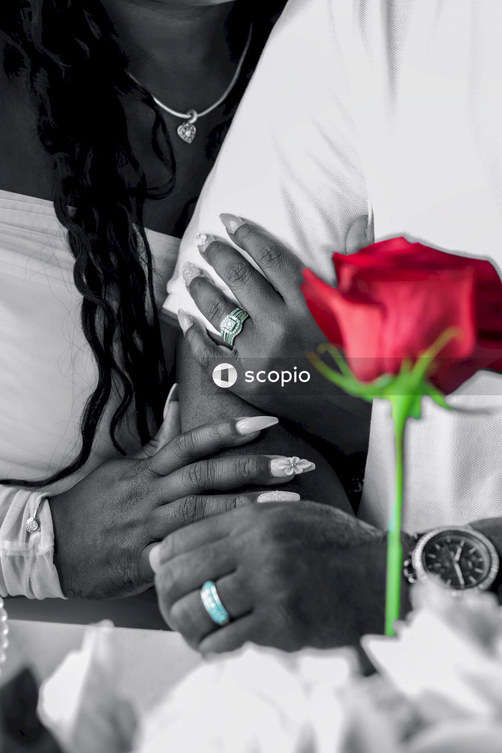 Grayscale photo of bride and groom linking arms and a red rose