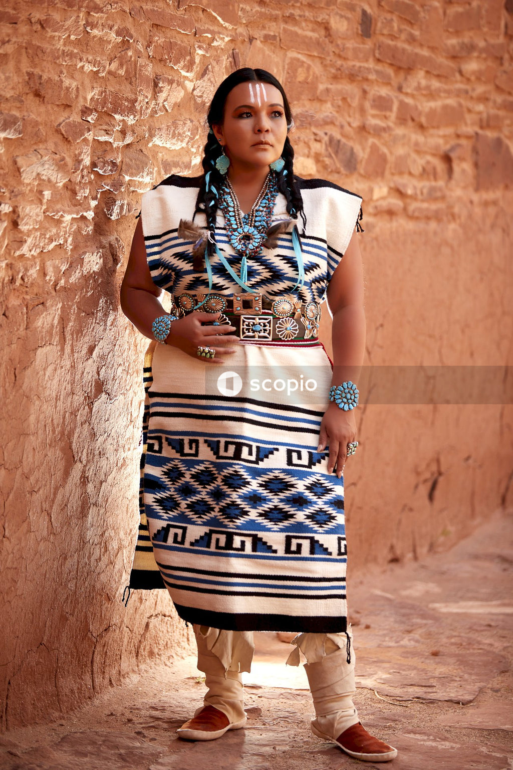Woman wearing traditional Indigenous American outfit standing beside canyon stone