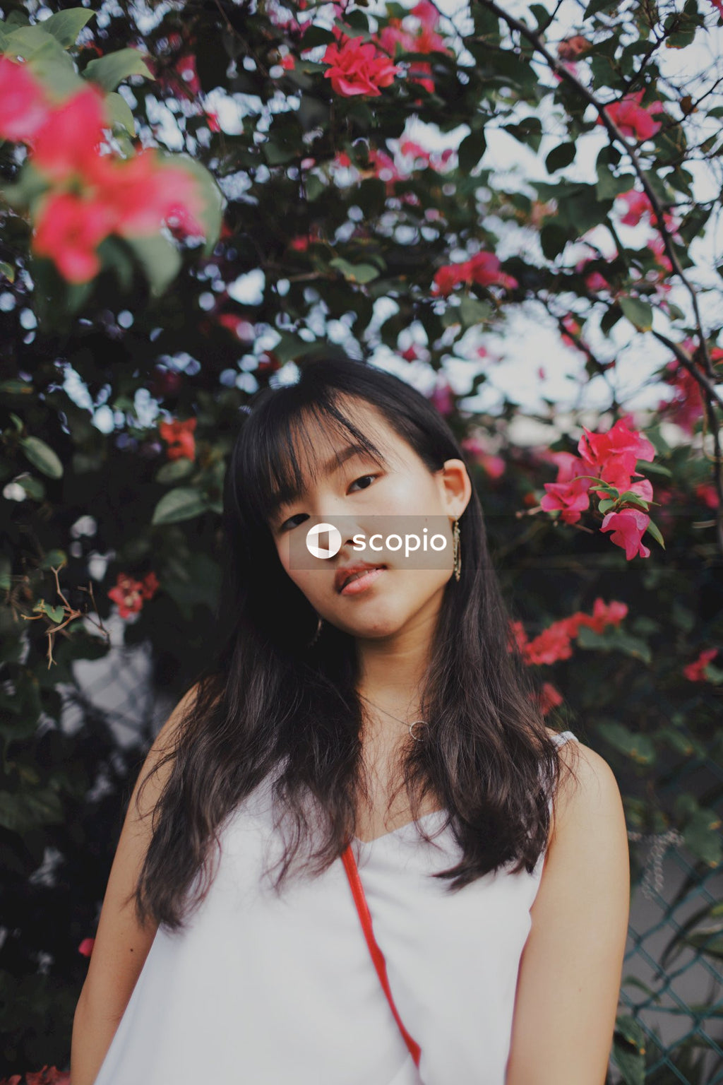Woman with bangs posing near flowers and bushes