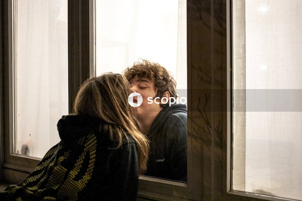 Young man and woman kissing with glass window separating them during Covid-19 pandemic