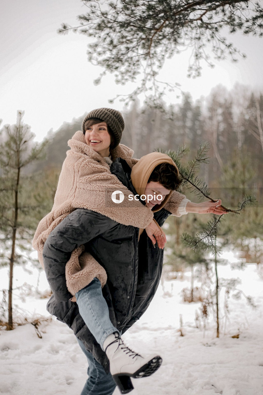 Young woman riding man's back in snow covered woods